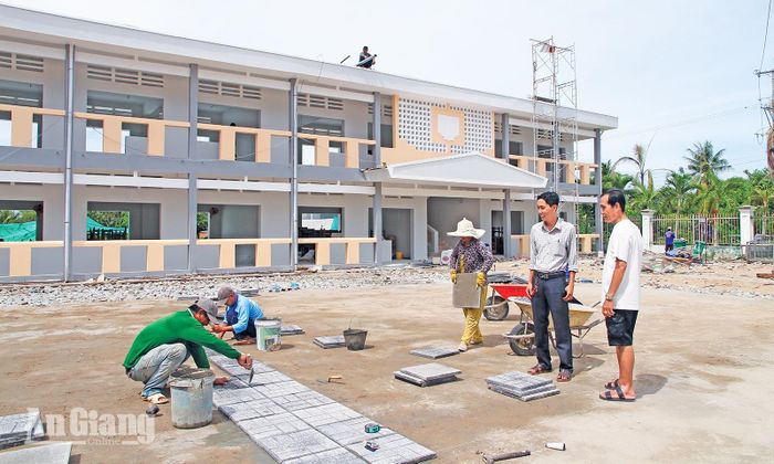 Công nhân lót gạch sân trường công trình cải tạo, nâng cấp Trường Trung học cơ sở Vĩnh Hòa, xã Vĩnh Xương. Ảnh: MINH HIỂN