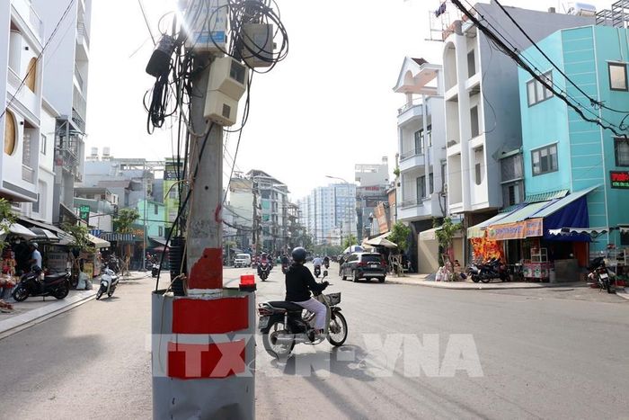 Trụ điện được bọc tôn, sơn phản quang và gắn đèn cảnh báo; phía trên vẫn còn nhiều dây điện và hộp kỹ thuật chằng chịt, gây mất mỹ quan. Ảnh: Tiến Lực - TTXVN
