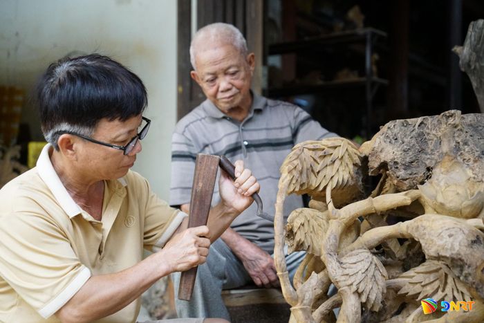 Nghệ nhân nhân dân Huỳnh Ri dõi theo từng đường đục của con trai (Nghệ nhân nhân dân Huỳnh Sướng). Ảnh: TRÂM ANH