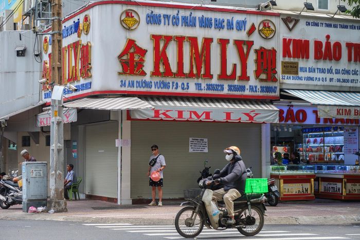  Cách đó 50 m là Công ty TNHH Vàng bạc và Đá quý Kim Lý. Theo thông báo, Kim Lý sẽ hoạt động trở lại sau một tháng kể từ ngày 14/7, hiện chỉ còn hơn một tuần nữa. Một người bốc vác, vận chuyển hàng hóa ở chợ An Đông cho biết thi thoảng vẫn có khách ghé đến, nhưng sau khi đọc thông báo dán trước cửa lại lặng lẽ rời đi. 