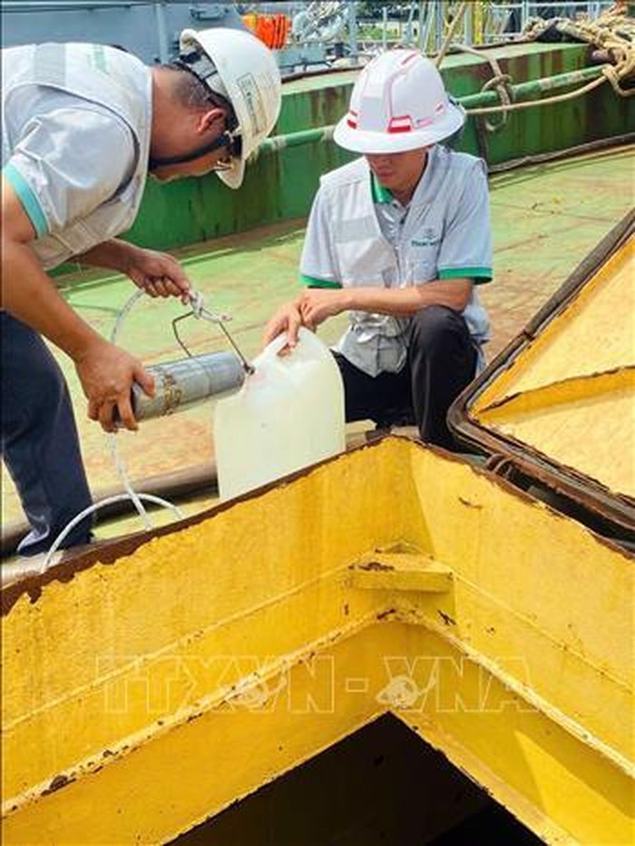 Lực lượng chức năng lấy mẫu dầu đi giám định. Ảnh: TTXVN phát