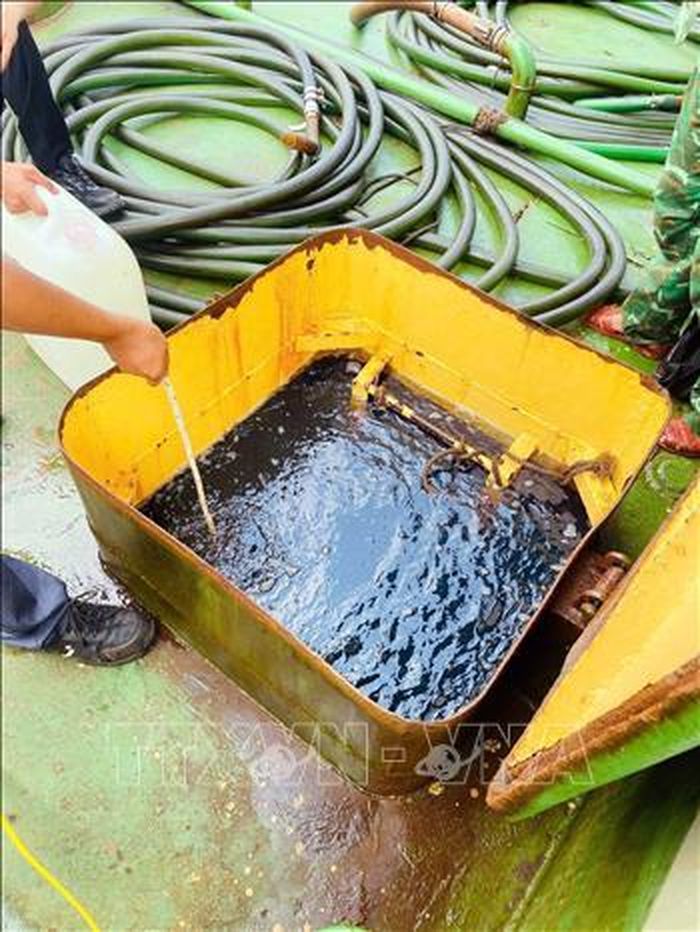 Lực lượng chức năng lấy mẫu dầu đi giám định. Ảnh: TTXVN phát
