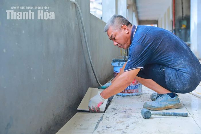 Công nhân thực hiện lát nền gạch hành lang dãy phòng học.