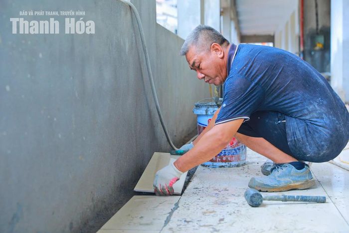 Công nhân thực hiện lát nền gạch hành lang dãy phòng học.