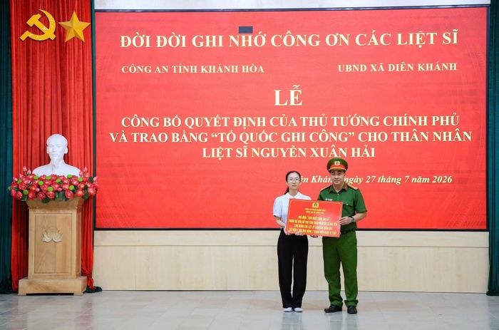 Thượng tá Nguyễn Vân Trường, Trưởng Công an xã Diên Lâm trao bảng tượng trưng nhận cho mẹ ruột cháu Nguyễn Thị Hải Yến - con gái liệt sĩ Nguyễn Xuân Hải để nhận cháu là con nuôi. Ảnh: Sơn Hồng.