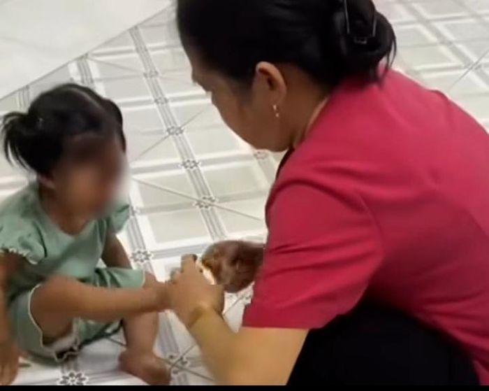 Bảo mẫu dùng giây thun tác động vào chân trẻ. (Ảnh cắt từ clip)