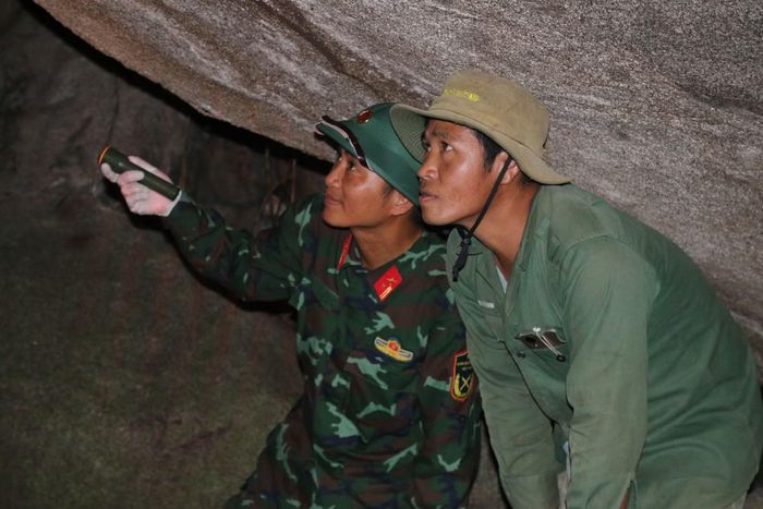 Anh Trương Công Bá (bên phải), người từng nhặt được cuốn sổ trong hang đá năm xưa hướng dẫn cán bộ, chiến sĩ Đội K51 tìm lại dấu vết trong hang đá.