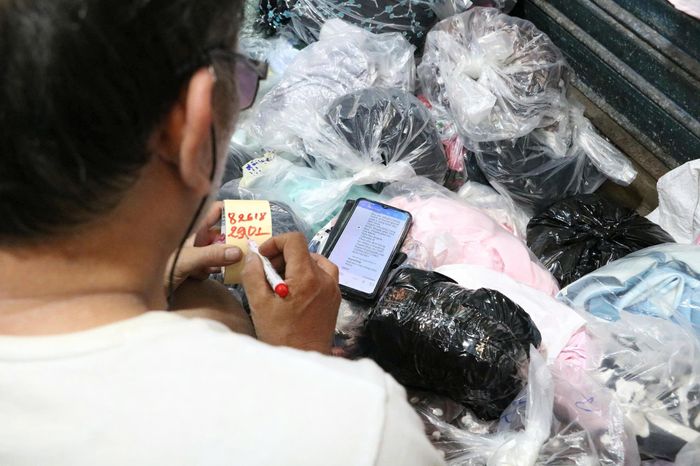 Người đàn ông tóc bạc ướm lên người những chiếc đầm sặc sỡ để khách hình dung rõ hơn về kiểu dáng sản phẩm.