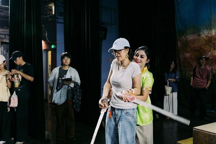 Nghệ sĩ hướng dẫn khán giả trẻ cách cầm và điều khiển đạo cụ sân khấu. Những hoạt động tương tác trực tiếp giúp nghệ thuật truyền thống trở nên gần gũi hơn, đồng thời tạo thêm giá trị cho các sản phẩm du lịch văn hóa về đêm. Ảnh: Phạm Tuấn Anh - TTXVN