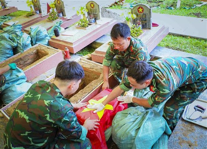Cán bộ, chiến sĩ phủ cờ Tổ quốc lên phần hài cốt liệt sĩ trước khi tiến hành các công đoạn tiếp theo. Ảnh: Xuân Tư - TTXVN