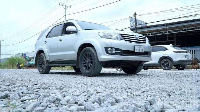 Xe ô-tô di chuyển qua đoạn đường rải đá lởm chởm làm cuốn lên bụi bẩn mù mịt, ảnh hưởng lớn đến đời sống người dân hai bên tuyến. (Ảnh: HỮU TÙNG)