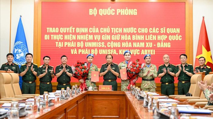 Hai sĩ quan nhận quyết định và hoa chúc mừng tại buổi lễ. Ảnh: VIẾT CHUNG