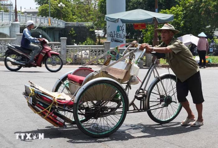 Nhọc nhằn đẩy xe xích lô lên dốc giữa nắng nóng gay gắt ở gần cầu Gia Hội, phường Phú Xuân, thành phố Huế. (Ảnh: Nguyên Lý/TTXVN)