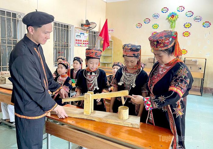 Giáo viên, Tổng phụ trách Đội Nguyễn Đình Kỷ cùng giáo viên Điểm trường Đá Bàn, trường Tiểu học Y Bằng, phường Mỹ Lâm hướng dẫn học sinh tìm hiểu mô hình cối giã gạo của đồng bào dân tộc thiểu số.