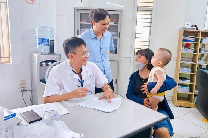 Giám đốc Trạm Y tế xã Đan Phượng Nguyễn Gia Phúc thăm hỏi, động viên phụ huynh đưa trẻ đến khám bệnh. Ảnh: TYT