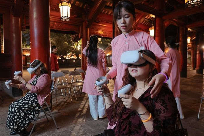 Khách du lịch trải nghiệm viết thư pháp bằng kính thực tế ảo tại tour đêm Văn Miếu – Quốc Tử Giám. Ảnh: Phạm Tuấn Anh - TTXVN