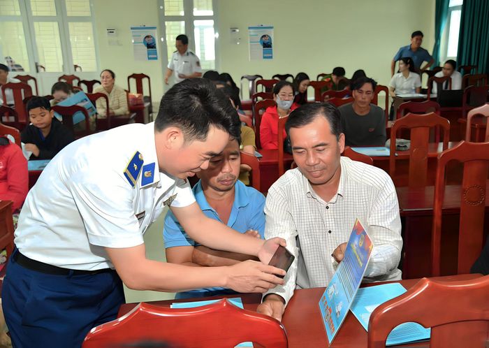 Cán bộ Bộ Tư lệnh Vùng Cảnh sát biển 4 phát tờ rơi, hướng dẫn bà con ngư dân quét mã QR tra cứu các quy định pháp luật. Ảnh: Đức Thái