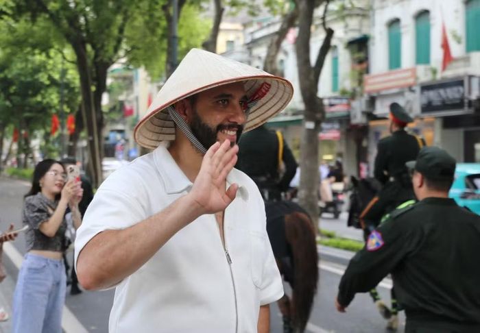 Một du khách nước ngoài đội nón lá Việt Nam vẫy tay chào đoàn diễu hành
