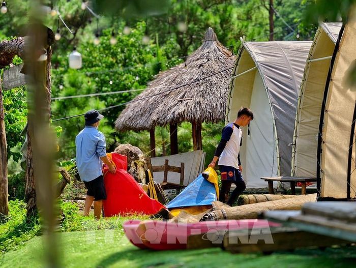Người dân di chuyển lều bạt, tài sản ra khỏi khu vực giải tỏa; phía sau là phương tiện được huy động tháo dỡ công trình vi phạm. Ảnh: Trung Nguyên - TTXVN