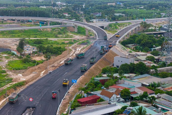  Hàng chục xe ben chở bê tông nhựa nóng xếp hàng chờ tới lượt đổ những lớp nhựa cuối cùng trên 2 nhánh đường dẫn. 