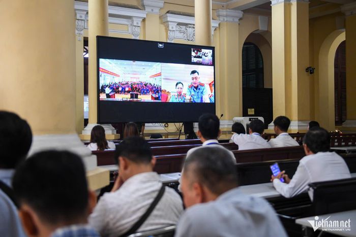 Những người có quyền, nghĩa vụ liên quan theo dõi phiên tòa qua màn hình đặt trước tòa án.