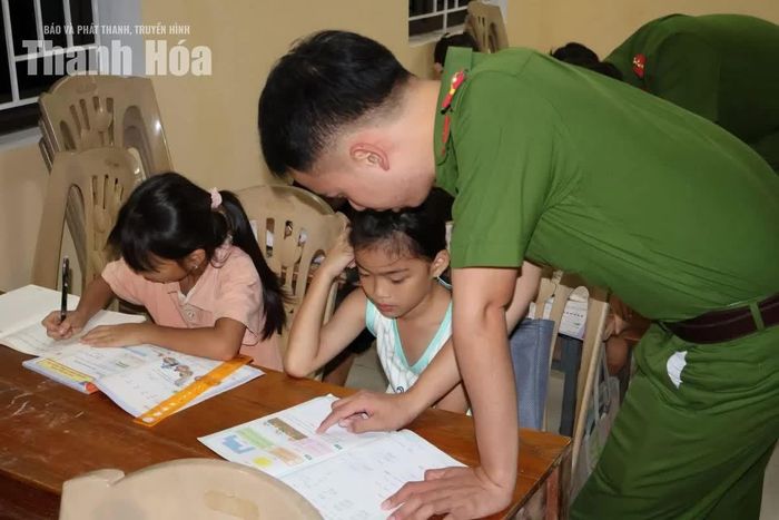 Cán bộ Công an xã Lương Sơn hướng dẫn học sinh làm bài tại “Lớp học 0 đồng” ở nhà văn hóa thôn Ngọc Quang.