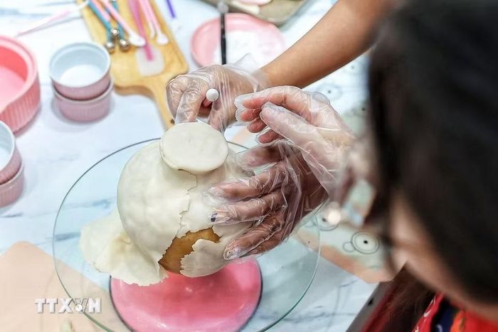 Người làm tỉ mỉ miết, chỉnh từng phần bột phủ bên ngoài của bánh Trung Thu để hoàn thiện hình dáng chiếc bình trước khi trang trí và kết hợp với những cành hoa tò he. (Ảnh: Phạm Tuấn Anh/TTXVN)