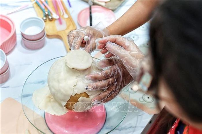 Người làm tỉ mỉ miết, chỉnh từng phần bột phủ bên ngoài của bánh Trung thu để hoàn thiện hình dáng chiếc bình trước khi trang trí và kết hợp với những cành hoa tò he.