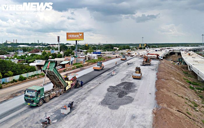 Nhiều xe ben chở bê tông nhựa nóng xếp hàng chờ thi công các lớp mặt đường cuối tại hai nhánh dẫn.
