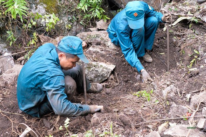 Dân quân dùng xà beng tìm kiếm giữa nền đất đá trên sườn núi. Ảnh: Tuấn Anh