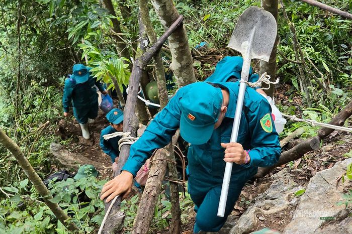 Chiến sĩ dân quân bám cây, vượt dốc mang dụng cụ lên điểm tìm kiếm. Ảnh: Tuấn Anh
