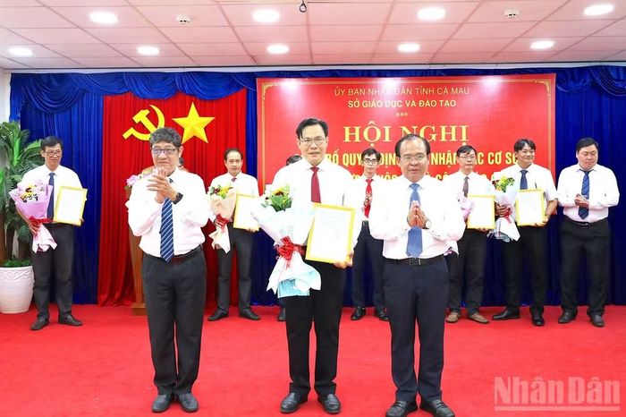 Phó Chủ tịch Ủy ban nhân dân tỉnh Cà Mau Nguyễn Minh Luân (bìa phải, hàng đầu tiên) trao quyết định bổ nhiệm và tặng hoa chúc mừng thầy Phạm Việt Hưng (đứng giữa), Hiệu trưởng Trường trung học phổ thông Đầm Dơi. (Ảnh: HỮU TÙNG)