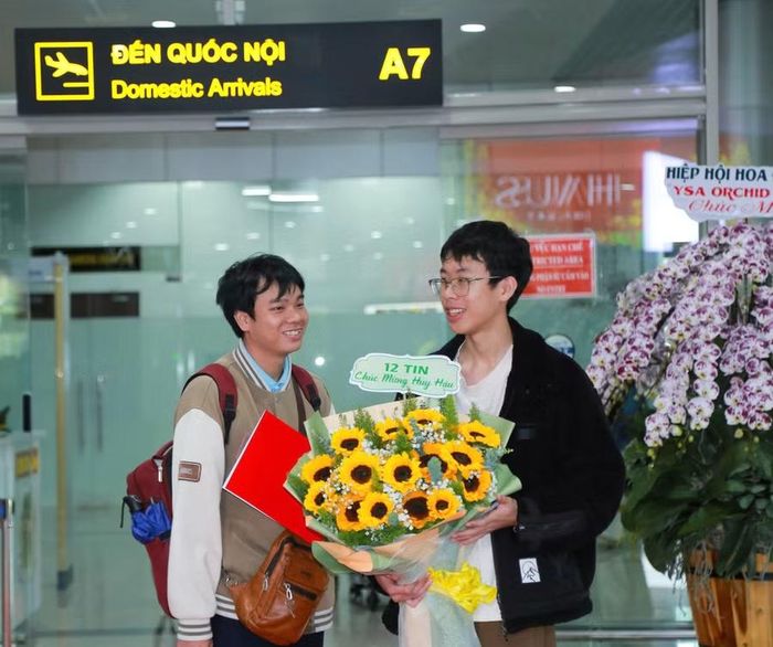 Bạn bè đón, tặng hoa và chúc mừng em Đặng Huy Hậu (bên trái) trở về sau khi xuất sắc giành Huy chương Bạc tại Kỳ thi Olympic Tin học Quốc tế (IOI) năm 2026.