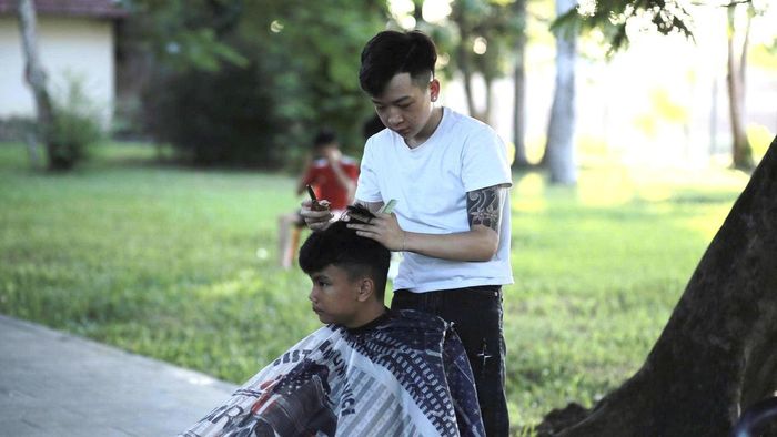 Người thợ trẻ chăm chú cắt tóc cho một em nhỏ tại góc cắt tóc miễn phí. (Ảnh: Nhật Quân)