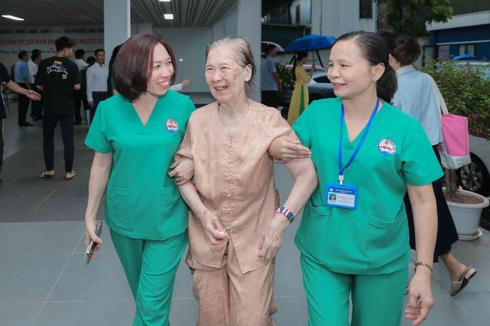 Cụ Vũ Thị Tuấn được nhân viên y tế hỗ trợ di chuyển để kiểm tra sức khỏe trước khi vào phòng sinh hoạt chung tại cơ sở số 1, ngõ 307 Thạch Bàn, Long Biên. Ảnh: Phan Phương – TTXVN