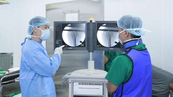  Ê-kíp can thiệp dưới sự hỗ trợ của hệ thống X-quang tăng sáng C-arm. (Ảnh: SỸ HIẾU) 