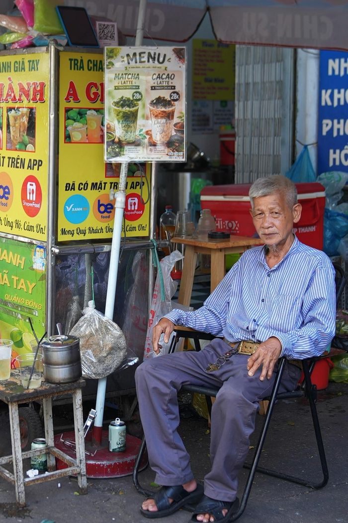  Hình ảnh người đàn ông lớn tuổi mặc áo sơ mi ngồi cạnh xe nước đã quen thuộc với nhiều khách hàng.
