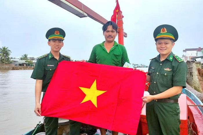 Thượng úy Nguyễn Trường Minh (bìa phải) cùng đồng nghiệp tặng cờ Tổ quốc cho ngư dân tàu cá trên địa bàn xã Đất Mũi, tỉnh Cà Mau. (Ảnh: ĐÌNH THẮNG)
