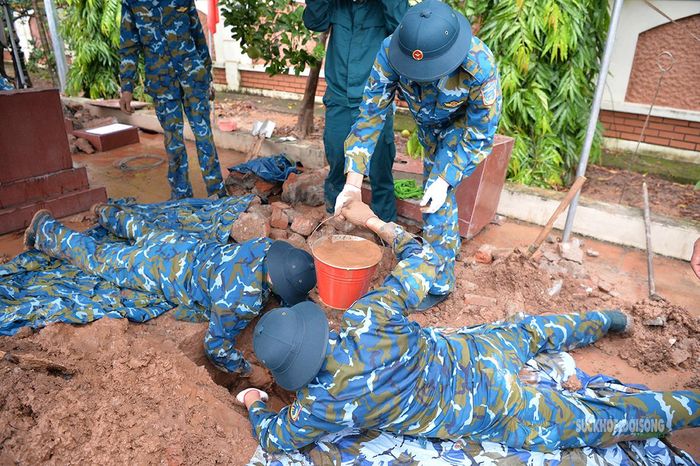 Chiến sĩ nằm sát mặt đất, đào và tát nước trong phần mộ. Ảnh: Tuấn Anh