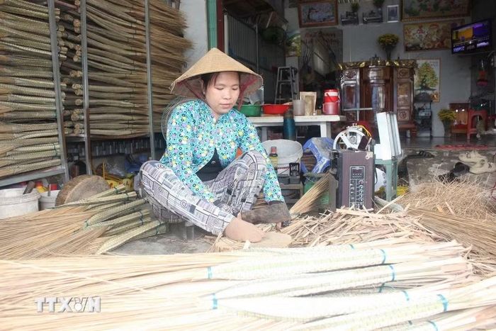 Người làm nghề thực hiện công đoạn bó mái chổi bằng những cọng dừa đã được sơ chế. (Ảnh: Thanh Sang/TTXVN)