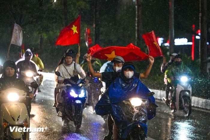 Nhiều người che ô, mặc áo mưa, trong khi không ít cổ động viên vẫn để mặc trời mưa, cầm cờ trên tay và hòa cùng dòng người. (Ảnh: Minh Sơn/Vietnam+)