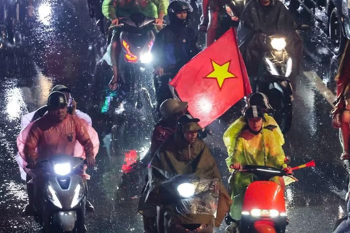 Dưới màn mưa nặng hạt soi rõ qua ánh đèn cao áp, người dân khoác lên mình đủ loại áo mưa và ra đường để ăn mừng chiến thắng của Đội tuyển bóng đá Nam Việt Nam