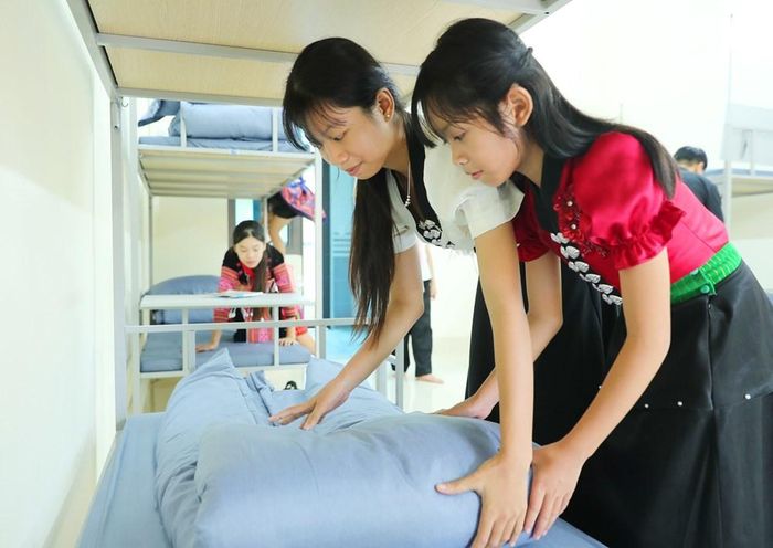 Hai học sinh cùng học cách gấp chăn, màn gọn gàng trong những ngày đầu làm quen với môi trường nội trú