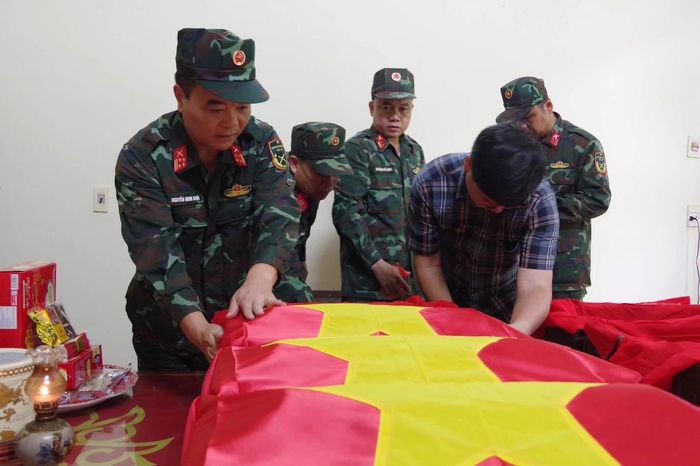 Đại tá Nguyễn Minh Khôi, Phó Chính ủy BCH Quân sự tỉnh Tuyên Quang, ông Lý Nam Thuỷ, Bí thư Đảng uỷ xã Minh Tân thực hiện nghi lễ đưa hài cốt liệt sĩ vào áo quan và phủ Cờ Tổ quốc. (Ảnh: BCHQS tỉnh Tuyên Quang)