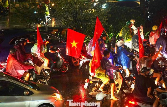 Áo mưa đủ màu hòa cùng sắc đỏ của cờ Tổ quốc, nhiều người mặc áo đội tuyển hòa vào dòng xe đang nối dài trên phố.