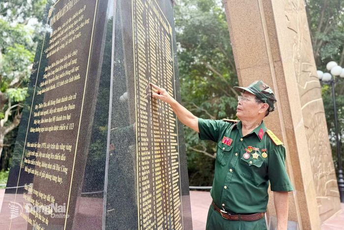 Cựu chiến binh Vũ Đức Ninh, nguyên Tiểu đội trưởng trinh sát, Trung đoàn Đặc công 113 bên những dòng tên đồng đội được khắc trên Nhà bia tưởng niệm liệt sĩ Đoàn Đặc công 113. Ảnh: N.Hạ