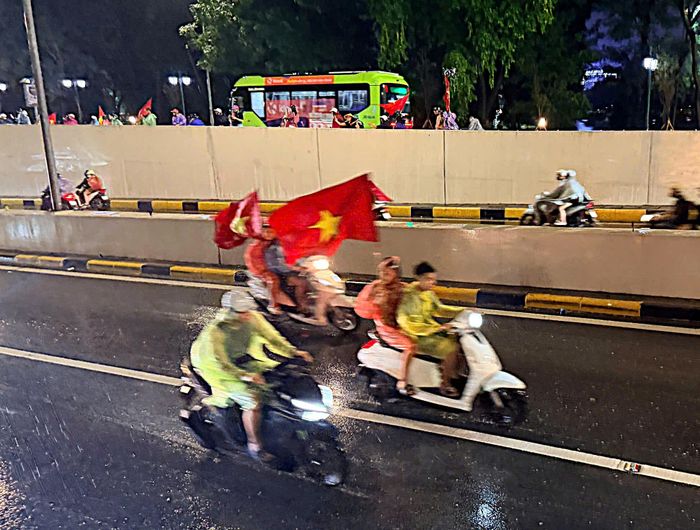 Không khí ăn mừng nhanh chóng lan rộng trên nhiều tuyến phố Hà Nội. Những tiếng hò reo, tiếng còi xe cùng sắc đỏ của cờ Tổ quốc tạo nên không khí sôi động giữa đêm mưa. (Ảnh ĐTĐH)