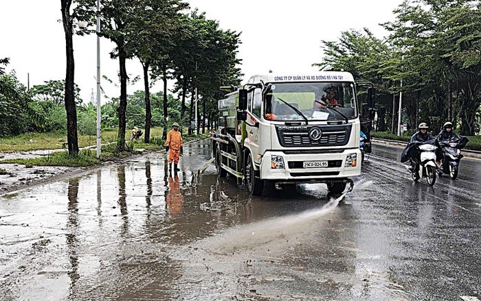 Công nhân sử dụng vòi phun cao áp để làm sạch mặt đường, cuốn trôi bùn đất và khơi thông hệ thống thoát nước. (Ảnh Thành Long)