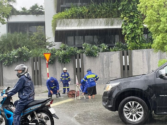 Tại tuyến đường Lê Hồng Phong, mực nước dâng cao, nhân viên môi trường được điều động đến hiện trường mở nắp cống, khơi thông dòng chảy. Ảnh: Thuỳ Dung