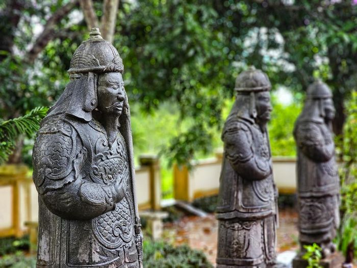Các vũ sĩ mang trang phục võ quan thời chúa Trịnh, đầu đội mũ tròn có chóp, thân mặc giáp, tay bồng gươm. Gương mặt trang nghiêm, râu dài, các chi tiết trên mũ, áo giáp và trang phục được chạm khắc chắc khỏe, công phu. Ảnh: Đình Minh